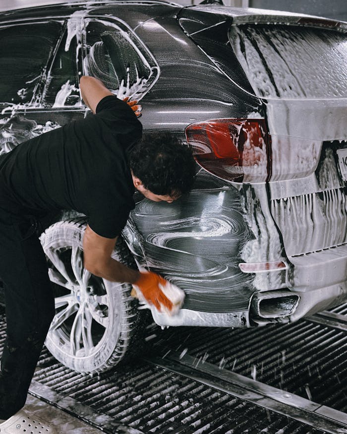 A person meticulously washing a car at a car wash using soap and a sponge.