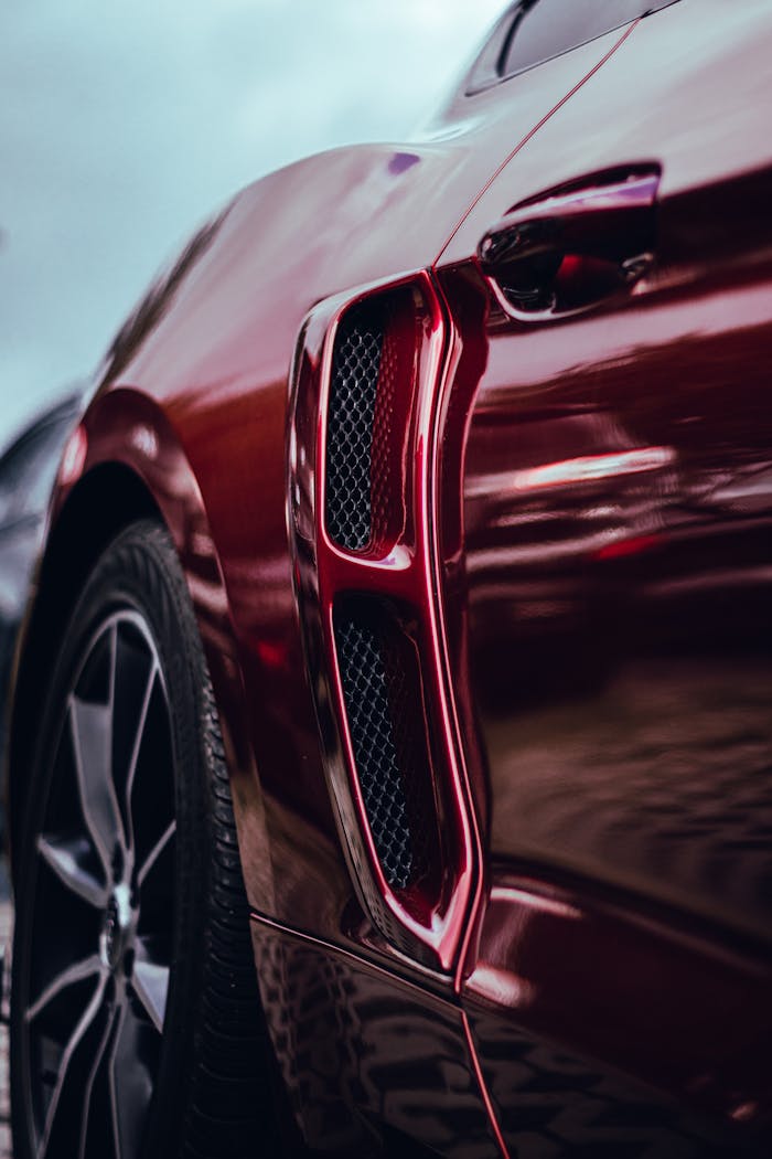 Detailed close-up of a luxury cars side vent and wheel showcasing sleek design and red color.
